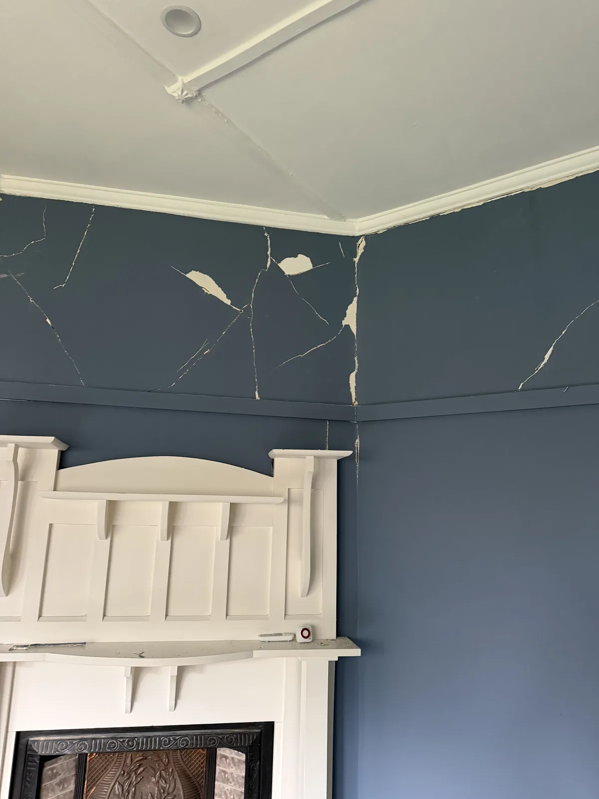 Blue interior wall above a white fireplace before repair, showing multiple visible cracks